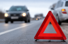 Ceļa malā novietota avārijas brīdinājuma zīme, fonā redzami pēc ceļu satiksmes negadījuma apstājušies automobiļi uz autoceļa.