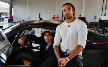Janns Mārdenboro (Jann Mardenborough) stāv pie sacīkšu automašīnas, kamēr otrs jaunietis sēž pie stūres autosporta boksos.